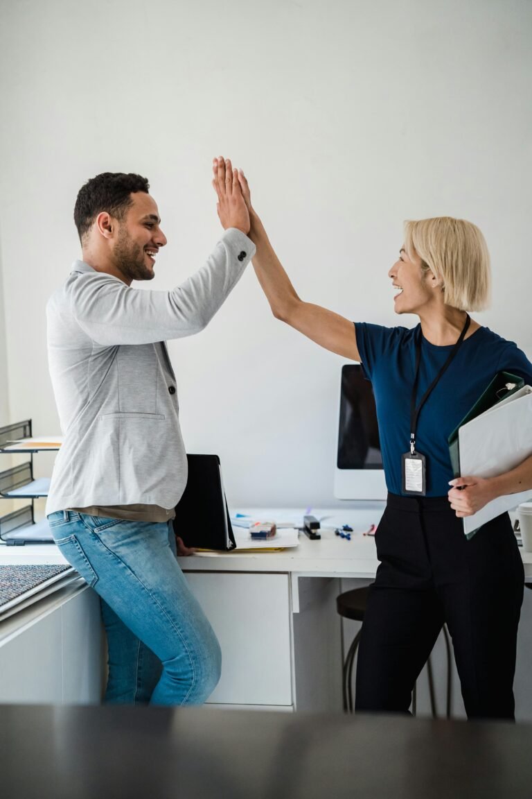 Two colleagues in an office exchanging a high-five, celebrating success.